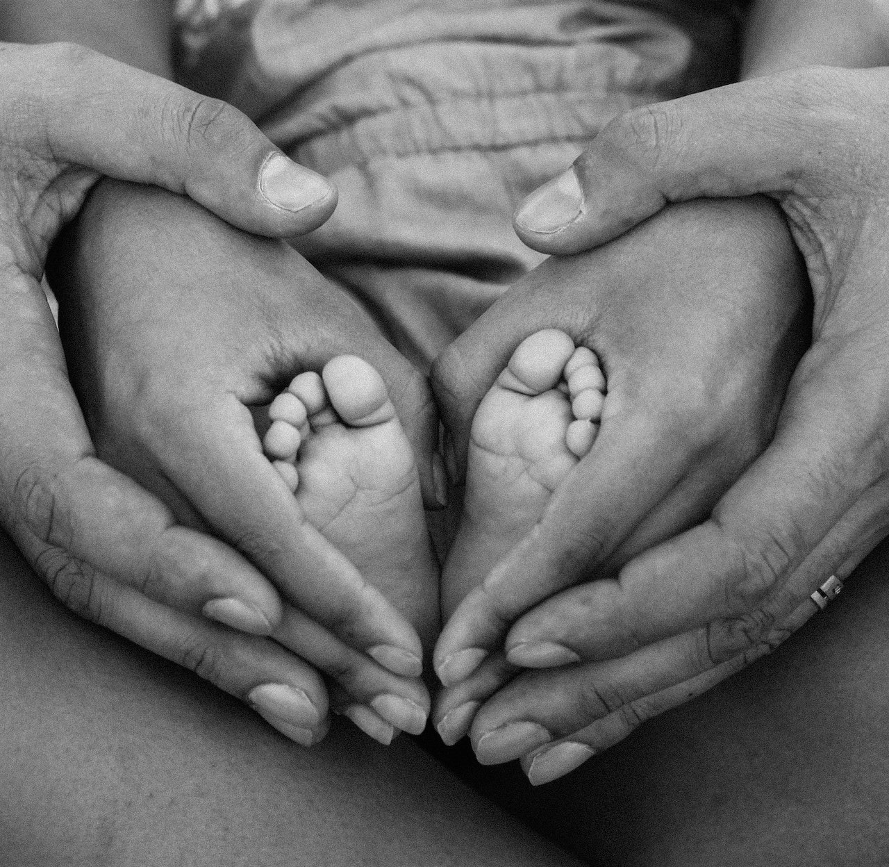 Mão de mãe acariciando ternamente os pequenos pés de seu bebê, simbolizando a cidadania Jus Solis através do nascimento.