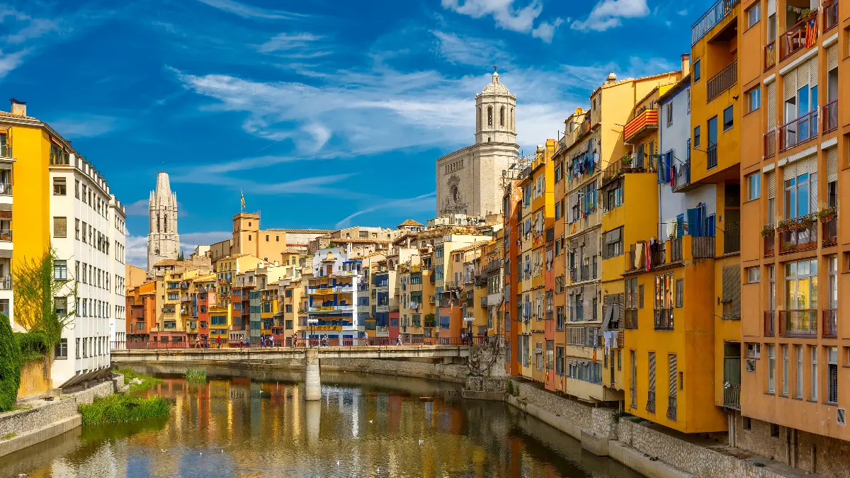 Vista panorâmica do Canal Onyar, na Catalunha, com casas coloridas em ambos os lados, refletindo suas fachadas nas águas calmas do canal.